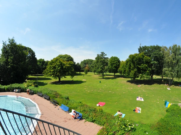 Liegewiese mit schattenspendenden Bäumen Blick vom Rutschenturm auf die Liegewiese im Freibad mit großen, schattenspendenden Laubbäumen