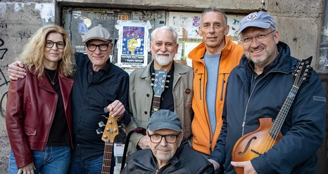 Eine Band aus sechs Mitgliedern lächelt in die Kamera.