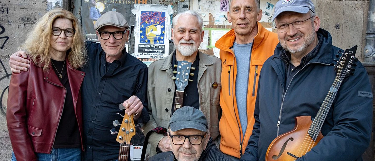 Eine Band aus sechs Mitgliedern lächelt in die Kamera.