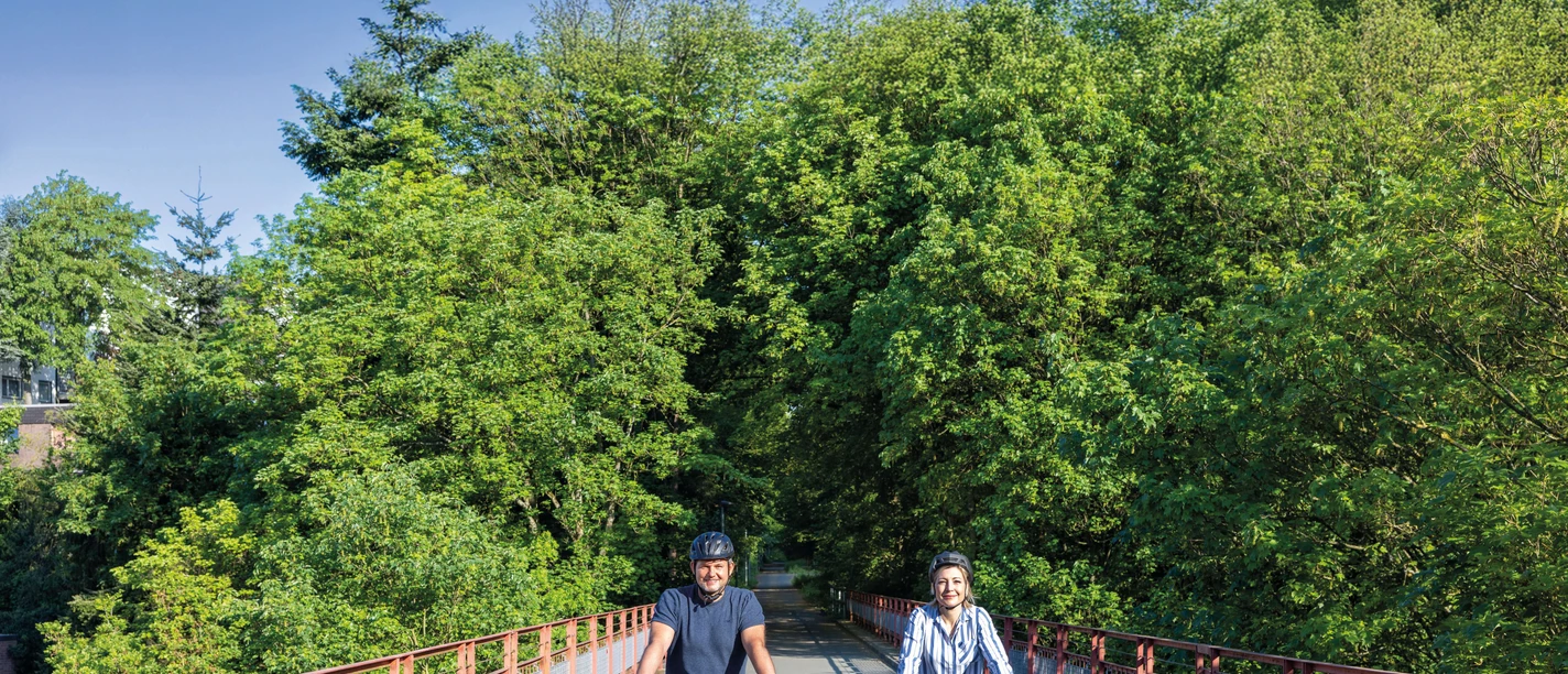 Viadukt Ruhrstraße Süd in Heiligenhaus Zwei Radfahrer_innen auf einer Brücke mit Bäumen und blauem Himmel.