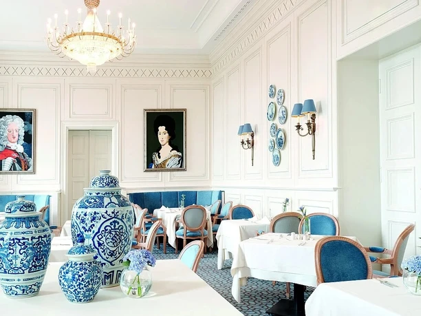 Pfingstbrunch Eleganter Speiseraum mit weißen Wänden, blauen Akzenten, Porzellanvasen und klassischer Dekoration.