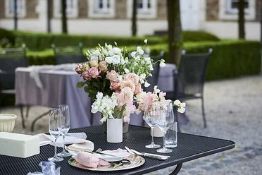Pfingstbrunch Festlich gedeckter Außentisch mit zarten Blumenarrangements und Gläsern im Hof.