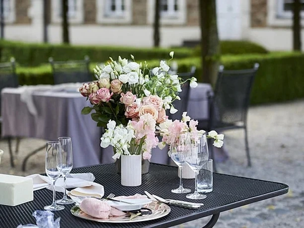 Pfingstbrunch Festlich gedeckter Außentisch mit zarten Blumenarrangements und Gläsern im Hof.