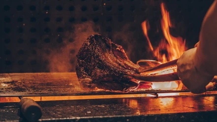 Spanish BBQ Friday Großes Stück Fleisch wird mit Zange über offenem Grillfeuer gegart