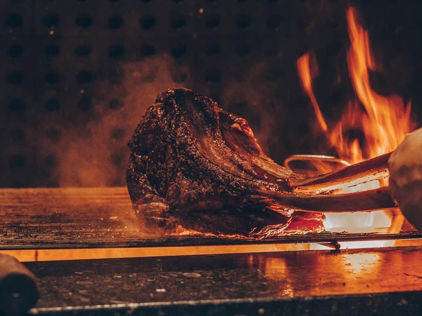 Spanish BBQ Friday Großes Stück Fleisch wird mit Zange über offenem Grillfeuer gegart