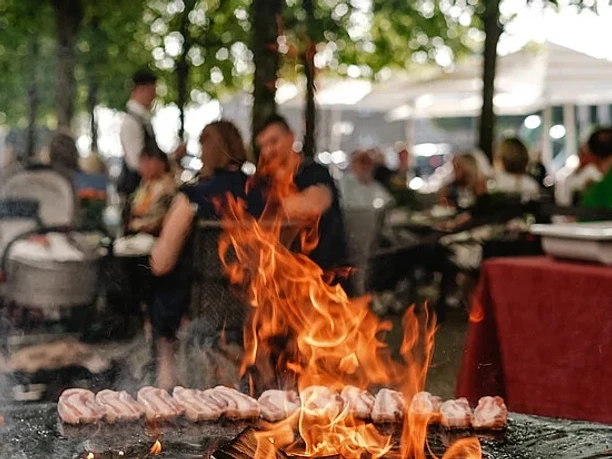 Spanish BBQ Friday Offenes Grillfeuer mit brutzelndem Fleisch vor einer belebten Außengastronomie