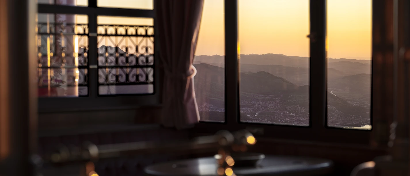 Royal Rigi Experience Sonnenuntergang über Bergketten, gesehen durch Restaurantfenster mit roten Vorhängen