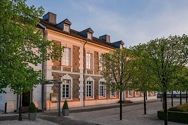 Mittagsmomente Vendome Fassade eines historischen Gebäudes im warmen Abendlicht, gesäumt von jungen Laubbäumen.