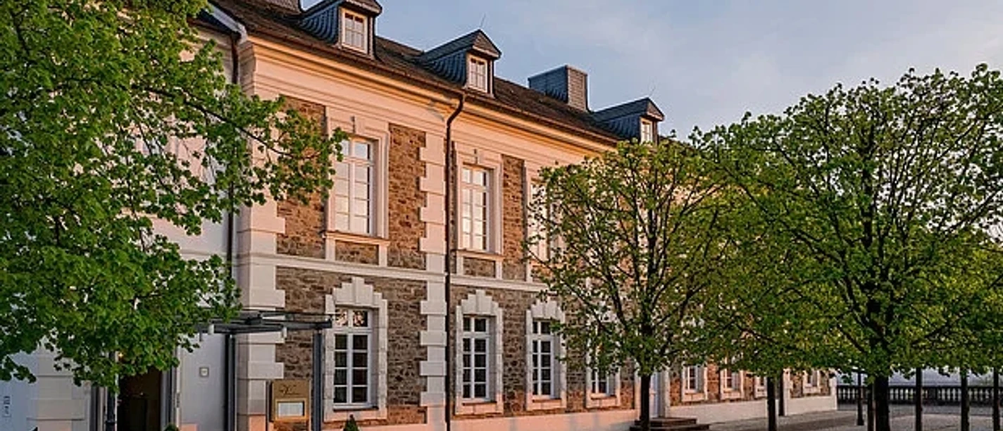 Mittagsmomente Vendome Fassade eines historischen Gebäudes im warmen Abendlicht, gesäumt von jungen Laubbäumen.