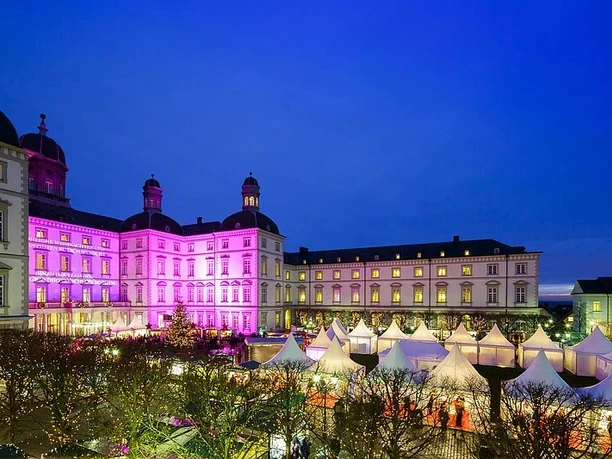 Unikat Weihnachtsmarkt Beleuchtetes Schloss mit pinker Fassade über weißen Marktzelten in der Abenddämmerung