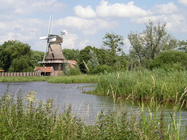 Hengstforder Mühle Die Hengstforder Mühle erhebt sich majestätisch mit ihren Flügeln inmitten grüner Natur am Flussufer.
