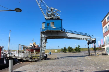 Elektrischer Halbportalkran Havenwelten im Sommer IMG_8644 (c) Tanja Mehl_Erlebnis Bremerhaven_WEB.jpg Ein blauer Halbportalkran am sonnigen Museumshafen überspannt den gepflasterten Weg.