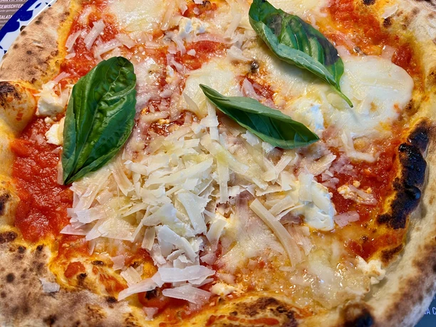 Pizza with tomato sauce, melted cheese, Parmesan shavings, and fresh basil.