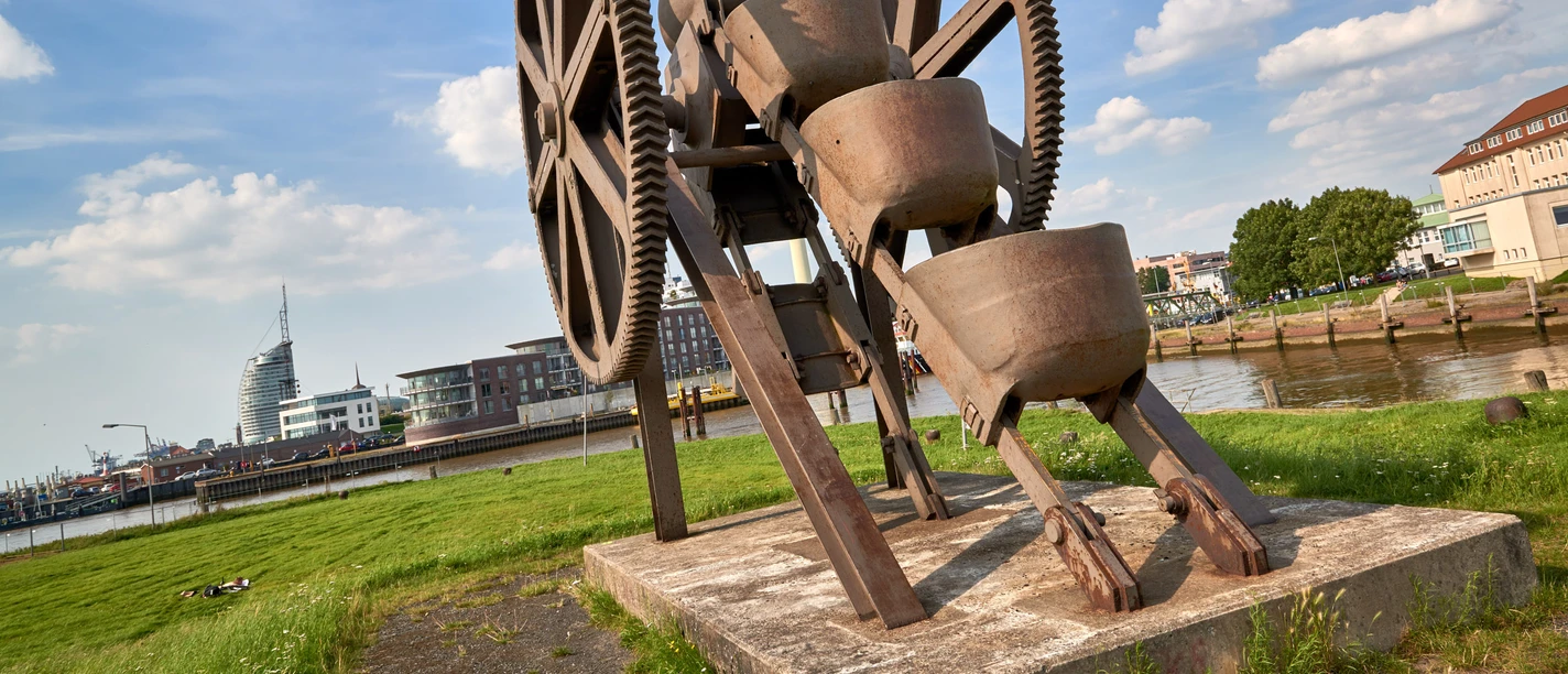 Stadtansichten von Bremerhaven Rostiger Eimerkettenbagger als Industriedenkmal am Ufer vor der Skyline von Bremerhaven.