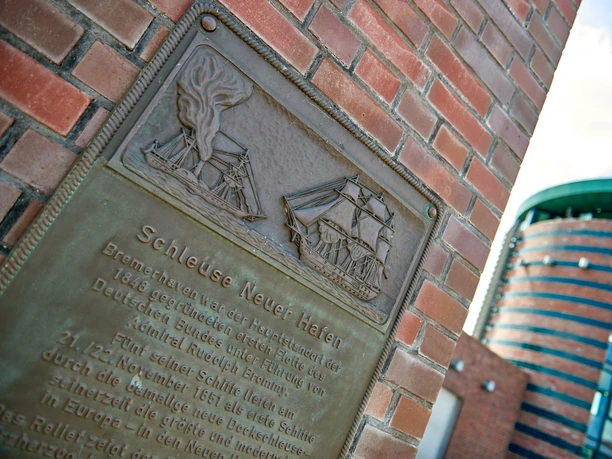 Stadtansichten von Bremerhaven Bronzene Gedenktafel der Schleuse Neuer Hafen mit Schiffsmotiven an einer Backsteinwand.