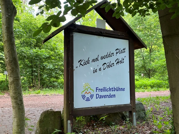 Roofed wooden sign for the Daverden open-air theater in the forest with a Low German slogan.