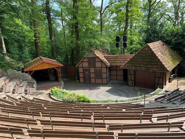 Daverden open-air stage Wooden rows of seats in front of an open-air stage with small half-timbered houses in the green forest.