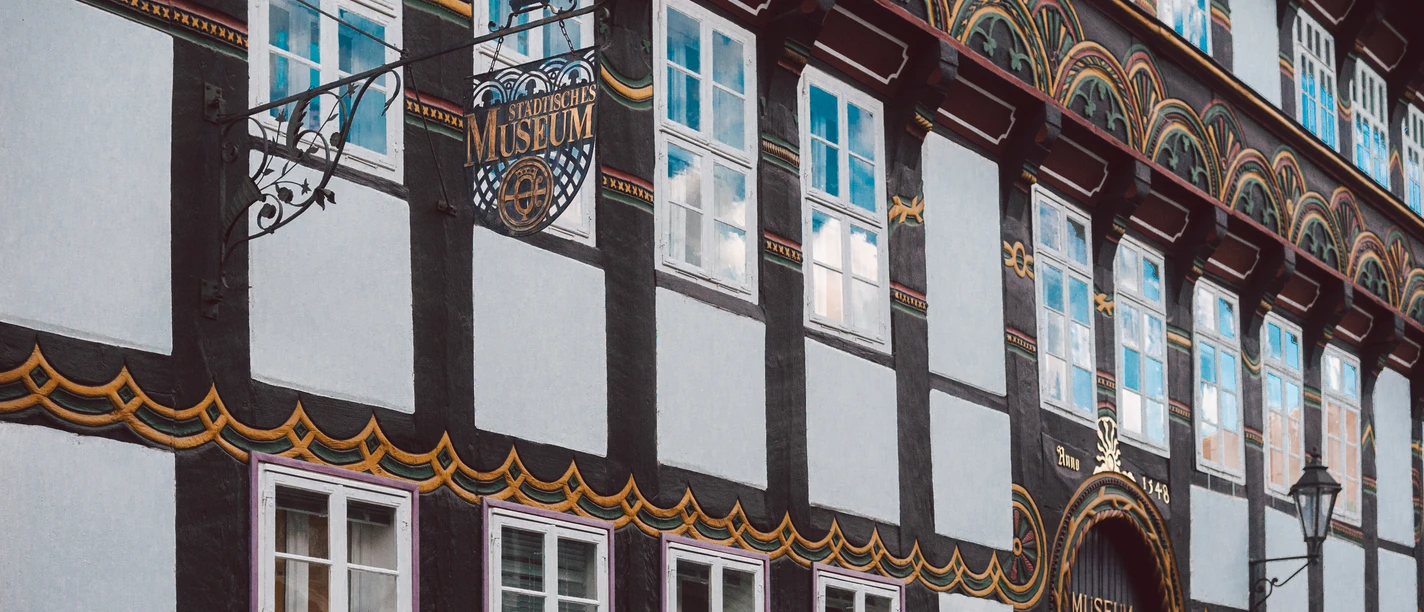 StadtMuseum 3, Einbeck - CC0.jpg Bunt verzierte Fachwerkfassade des Städtischen Museums Einbeck mit schmiedeeisernem Schild.
