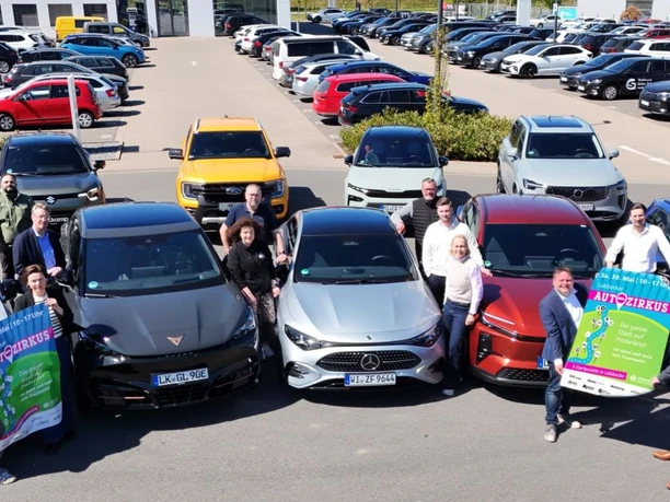 Autozirkus 2026 Gruppe von Personen mit Autos und Autozirkus-Plakaten auf großem Parkplatz