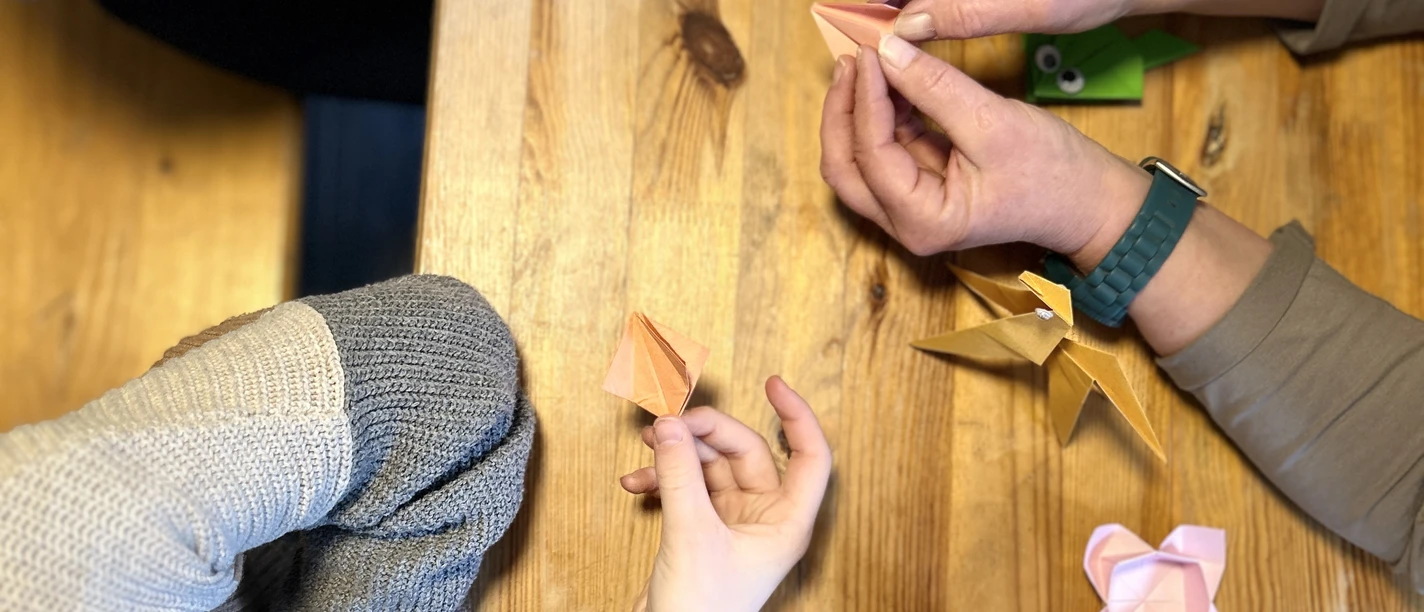 Origamitag Kinder und Erwachsene falten farbiges Origami an einem Holztisch.