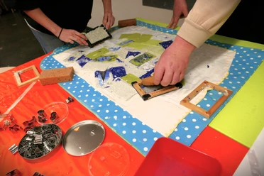 Kreatives_Papierschöpfen Hände beim kreativen Papierschöpfen mit Formen und farbigen Papierstücken auf Arbeitstisch