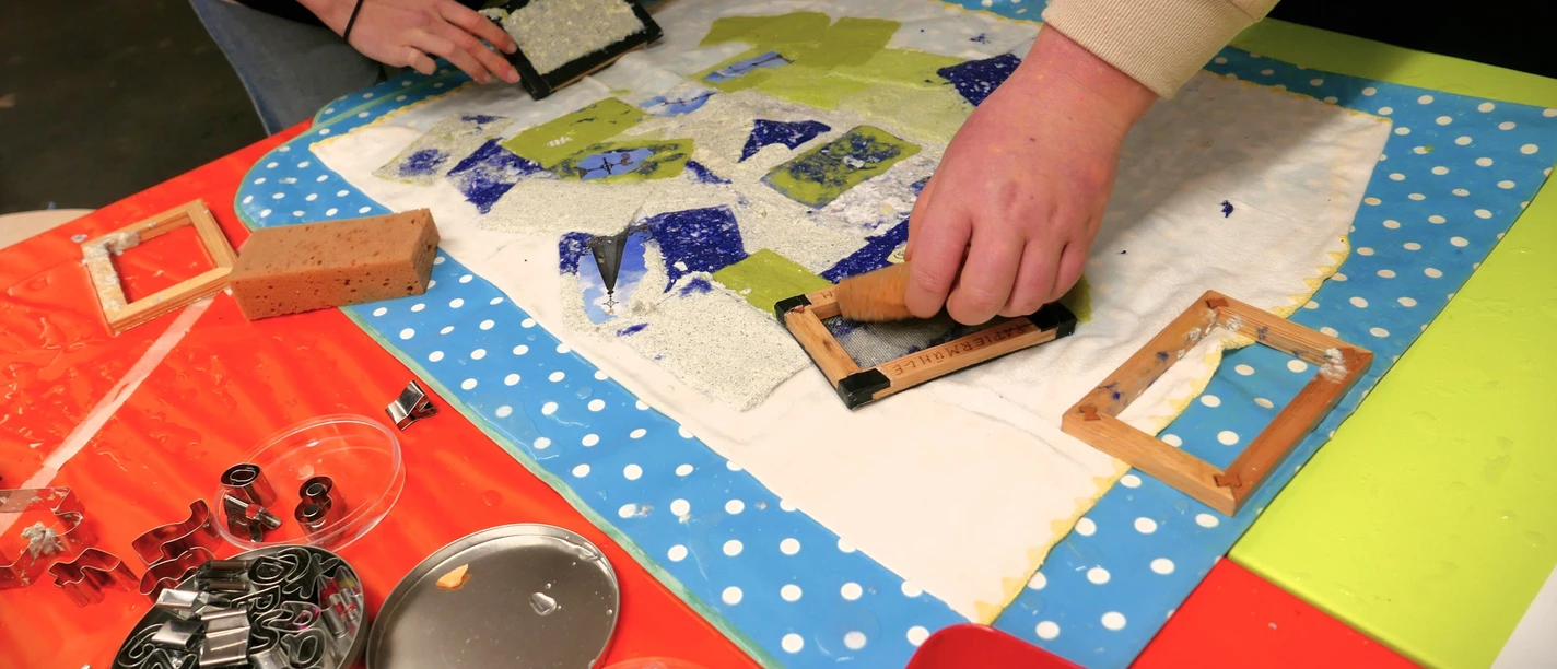 Kreatives_Papierschöpfen Hände beim kreativen Papierschöpfen mit Formen und farbigen Papierstücken auf Arbeitstisch
