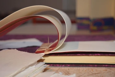 Aufgeschlagene Buchseiten und handgeschöpftes Papier liegen für die Buchbindearbeit bereit