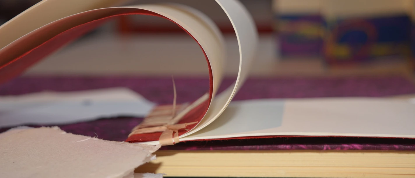Bücher Aufgeschlagene Buchseiten und handgeschöpftes Papier liegen für die Buchbindearbeit bereit