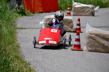 Header_optimized.png Jeune pilote en caisse à savon négociant un virage entre cônes et bottes de paille
