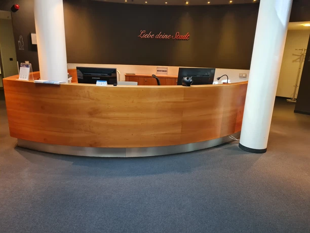 Geschwungener Empfangstresen aus Holz mit Monitoren vor dunkler Wand und weißen Säulen