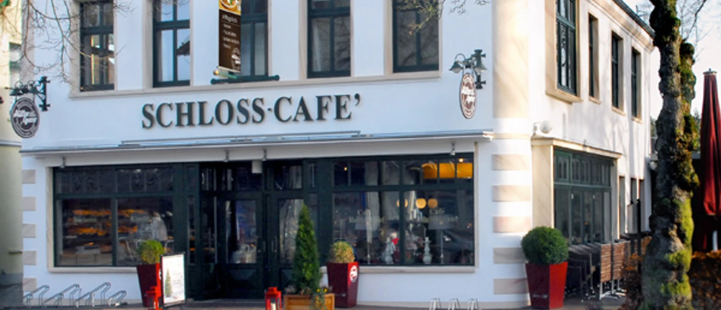 Aussenaufnahme vom Schloss-Café Zweistöckiges Gebäude mit heller Fassade und großen Fenstern, Eingang zum Schloss-Café.