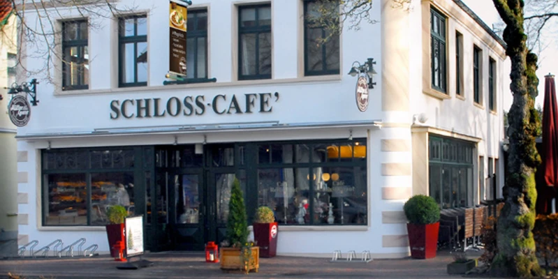 Aussenaufnahme vom Schloss-Café Zweistöckiges Gebäude mit heller Fassade und großen Fenstern, Eingang zum Schloss-Café.