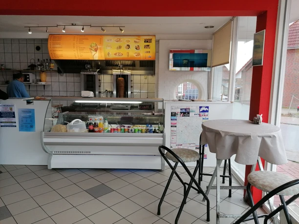 Verkaufsraum Heller Verkaufsraum mit Theke, Dönerspieß, Menütafel und Stehtisch am Fenster.