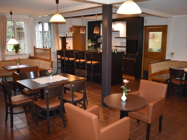 Gastraum Heller Gastraum mit dunklen Holztischen, braunen Stühlen, kleiner Theke und Rosen auf den Tischen.