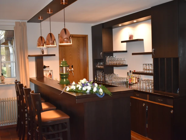 Thekenbereich Dunkelbraune Holztheke mit gepolsterten Barhockern, Zapfanlage und kupferfarbenen Hängelampen.