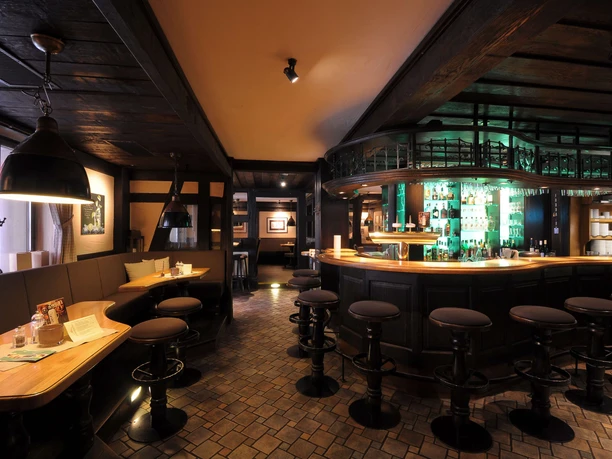 hotel-niedersachsen-sachsenklause Theke mit Barhockern rechte Bildseite, erhöhte Sitzmöglichkeiten und Tische linke Bildseite, Ausstattung in dunklem Holz