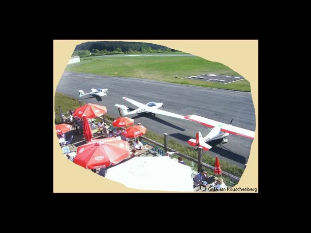 ab_cafeamraeuschenberg_terrasse.jpg Sonnenterrasse mit Sonnenschirmen und Flugzeuge in Parkposition