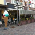 Großes Eiswaffel-Dekorationselement vor Eiscafé Mosena, umgeben von Außensitzplätzen und Blumenkästen.