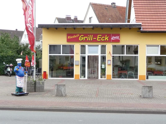 riedels-grilleck-aussen Außenansicht vom Imbiss, gelbes Haus mit Kochfigur am Straßenrand
