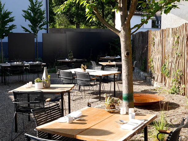Een ruim terras met houten tafels en zwarte metalen stoelen biedt een rustige plek om buiten te eten.