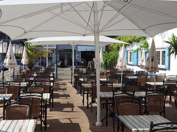 Sunny outdoor area of a café with empty tables and chairs under white parasols.