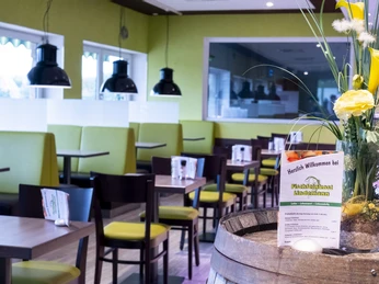 Ein modern gestaltetes Restaurant mit hellen, grünen Sitzbänken und einem Blumenarrangement.A modern restaurant with bright, green benches and a flower arrangement.En moderne restaurant med lyse, grønne bænke og et blomsterarrangement.Een modern restaurant met lichte, groene banken en een bloemstuk.