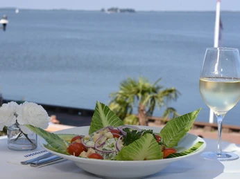 Essen Salat Ein frischer Salat mit Tomaten und Gurken auf einem Tisch mit Seeblick und einem Glas Weißwein.