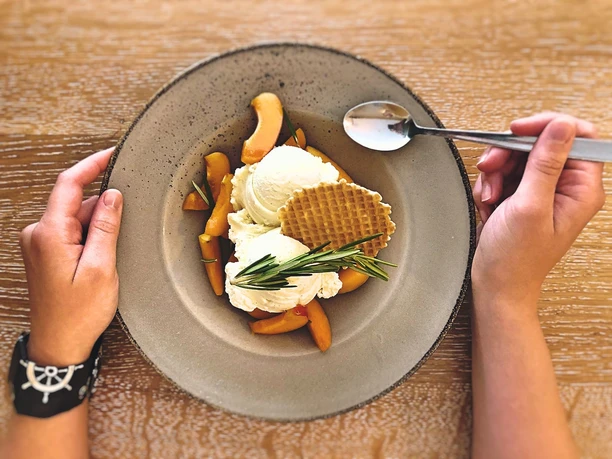 Vanille Eis Ein Teller mit Vanilleeis, Apfelschnitzen, einem Waffelblatt und Rosmarinzweig, von Händen gehalten.