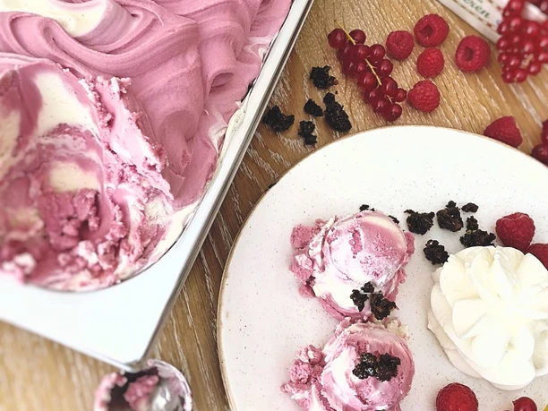 Eis mit Beeren Fruchtiges Himbeereis in eleganter Wellenform neben frischen Beeren und Schlagsahne auf einem Tisch.