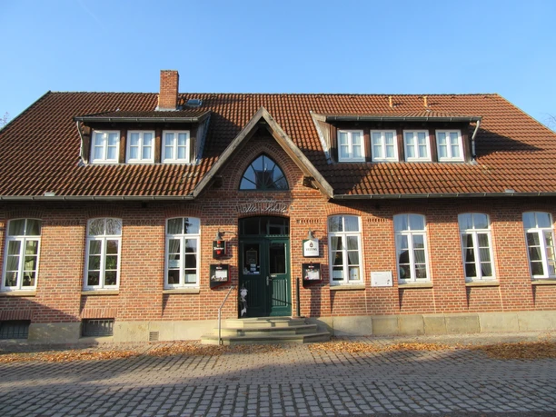 A brick building with high windows and signs above the entrance under a gabled roof.