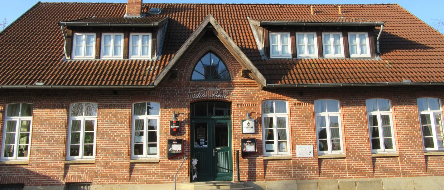Hotel & Restaurant Alte Schule A brick building with high windows and signs above the entrance under a gabled roof.