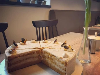 Eine angeschnittene Sahnetorte mit Schichten auf einem Teller in einem Café mit Vase im Hintergrund.