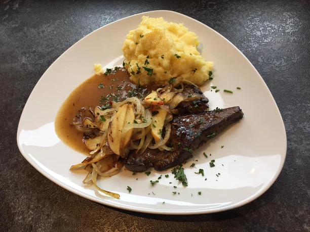 Tellergericht Saftiges Steak mit gebratenen Zwiebelringen, serviert mit cremigem Kartoffelpüree und Bratensoße.