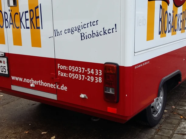 Café Honeck Seitliche Rückansicht eines roten Verkaufsanhängers der Biobäckerei Honeck auf gepflastertem Boden.